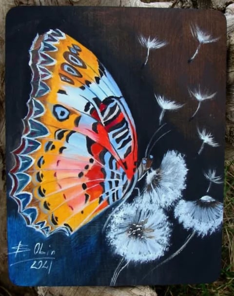 Hand-painted artwork on dark canvas featuring a colorful butterfly with yellow and red wings next to white dandelion seeds floating in the air